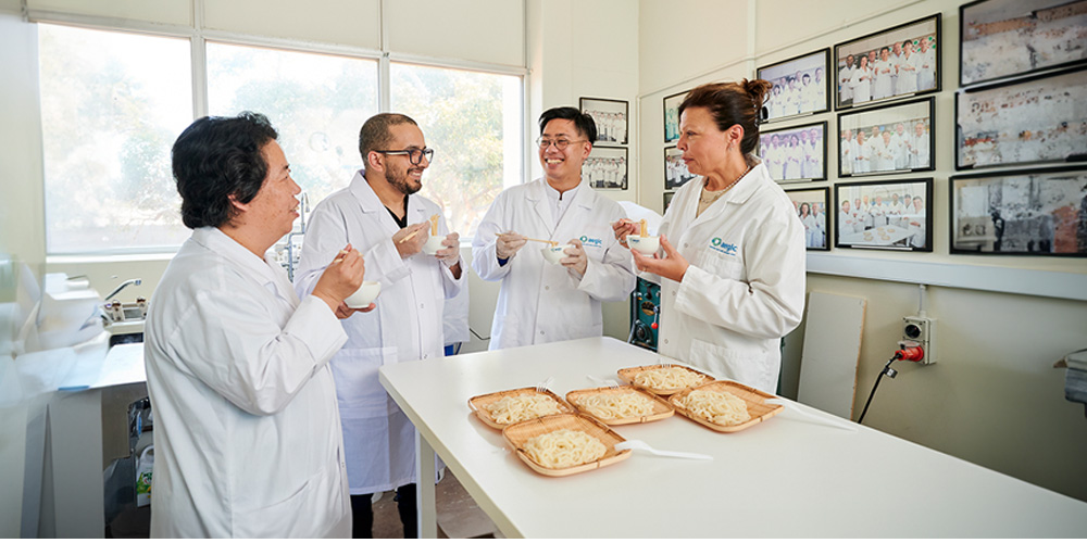 Four people in white lab coats in laboratory tasting noodles