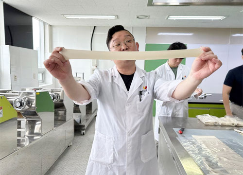 A man stands holding a stretched piece of noodle dough