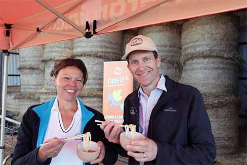 Dr Larisa Cato and Dr Dan Mullan stand in front of hay bales, each holding a bowl of noodles