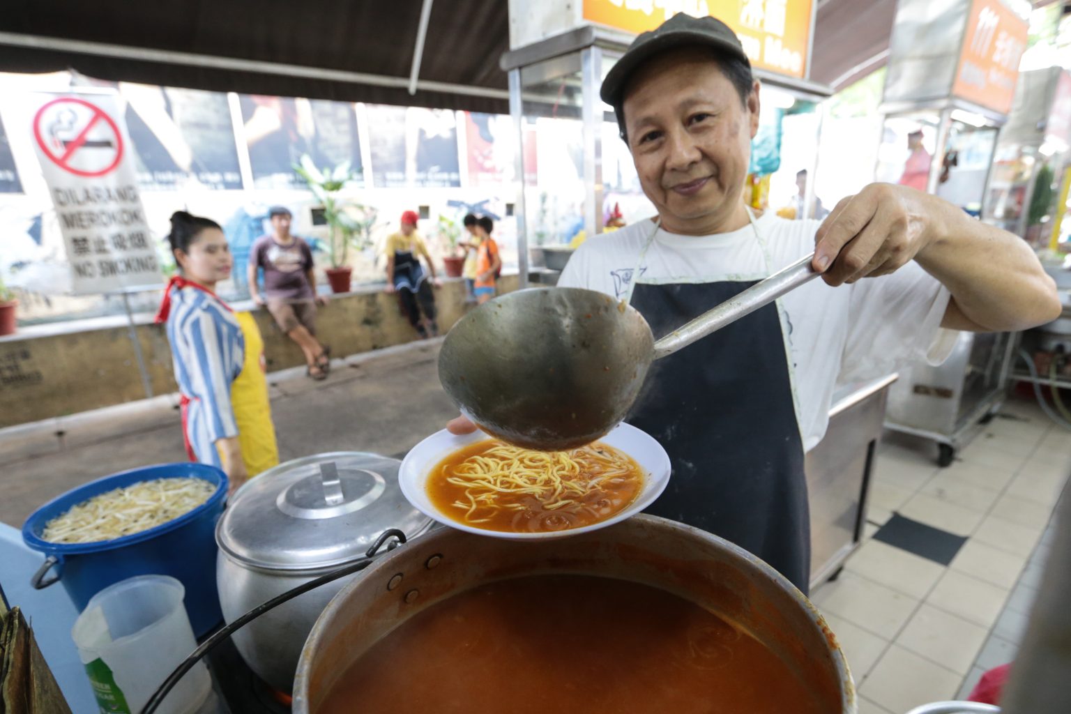 A street hawker pouring noodles into a bowl